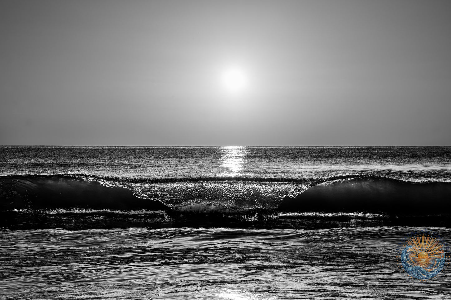 Black and white Coastal photograph of sunrise with ocean wave peelig off under a rising sun on the horizon.