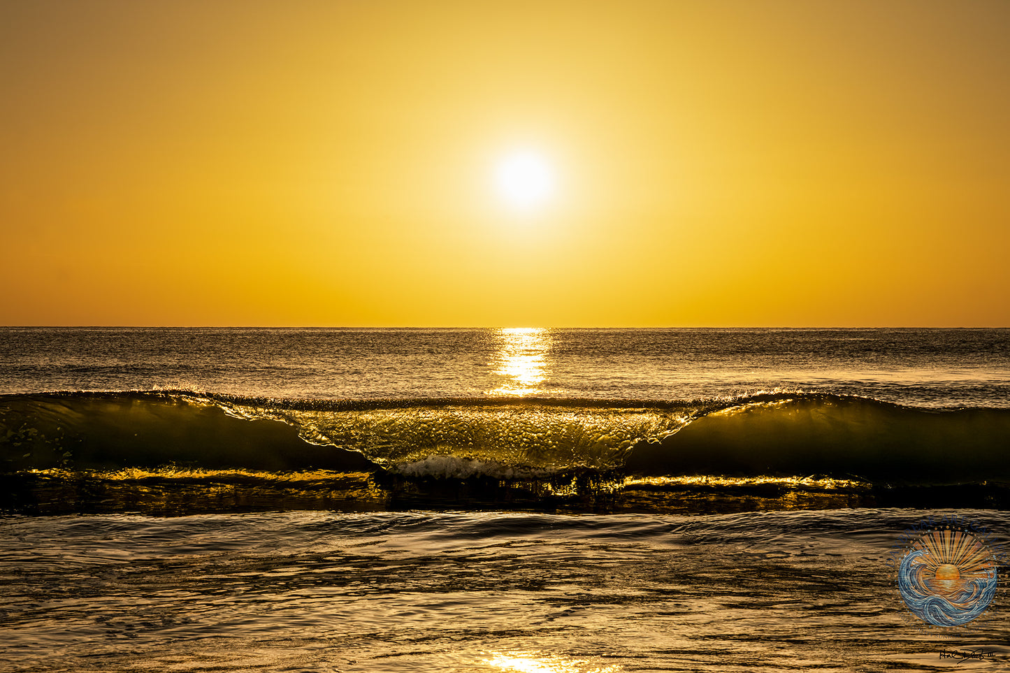 Golden sunrise over the ocean with a wave breaking in the foreground and the sun reflecting on the water surface.
