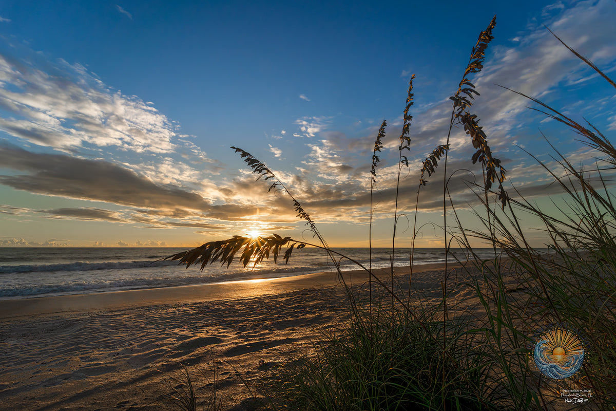 Sunrise over Playalinda Beach, Florida, September 9, 2026 — a sunburst breaking through clouds strung along the horizon, framed by sea oats