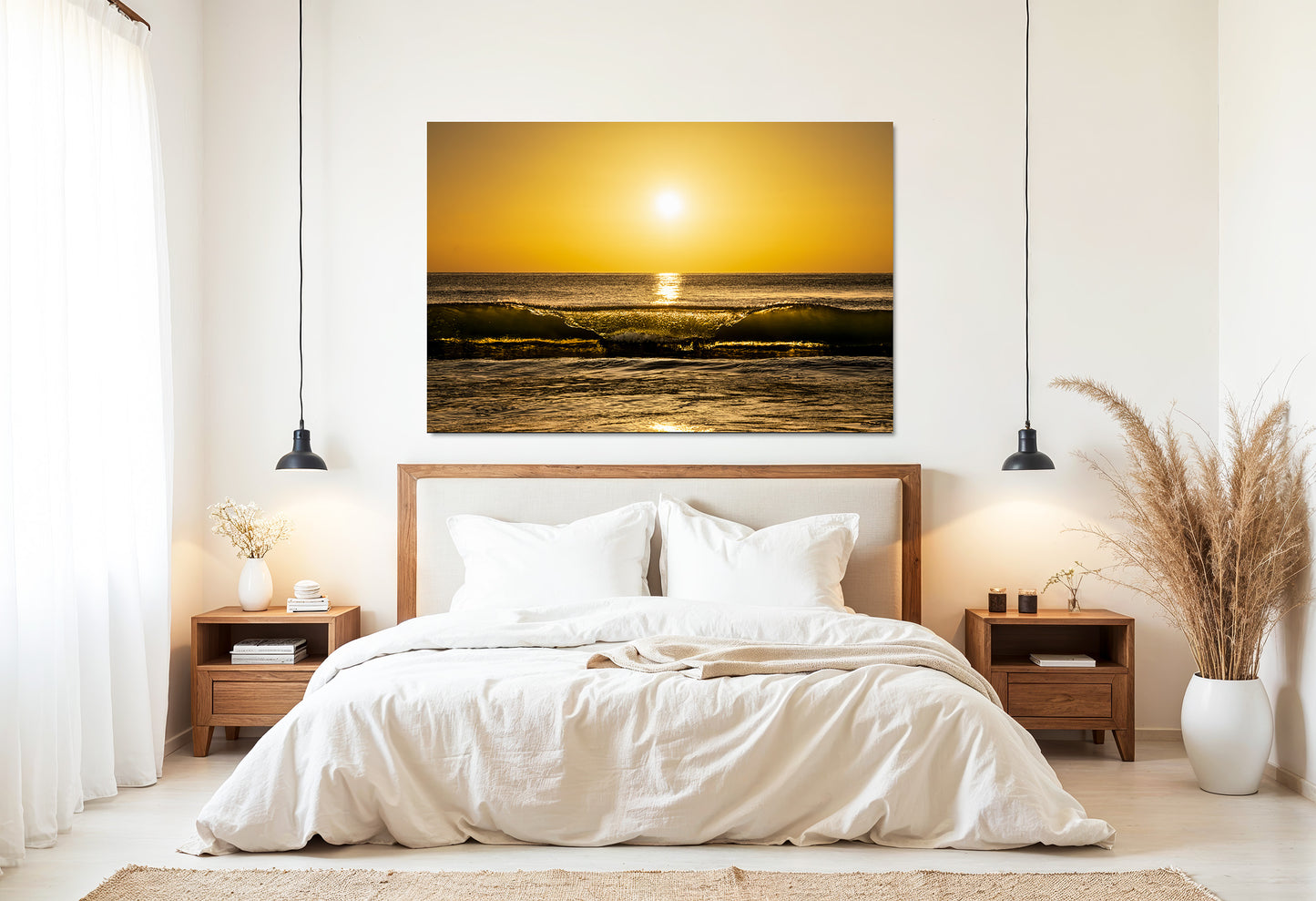 A rectangular wall art print showing a golden ocean sunset hangs above a neatly made bed in a bright, modern bedroom with wooden nightstands, pendant lights, and dried grass decor.