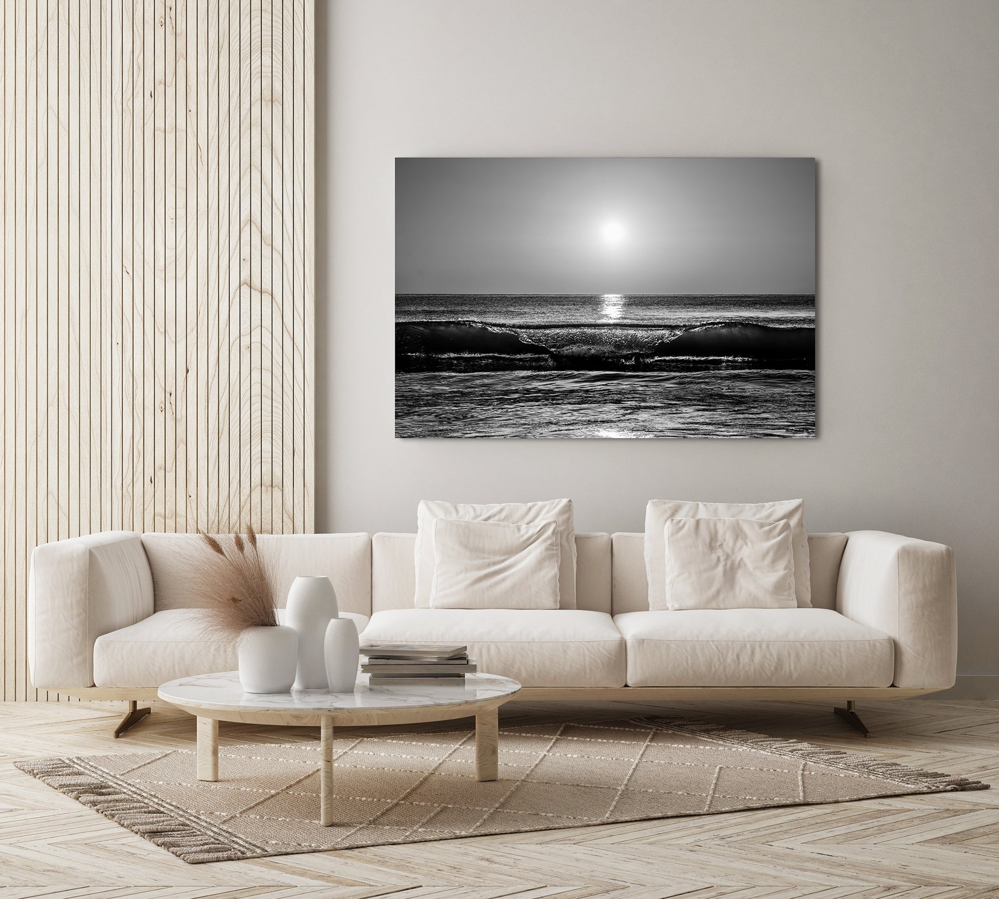 A black and white ocean wave photograph print displayed on a light gray wall above a modern cream-colored sofa in a minimalist living room setting.